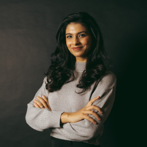 Aayushi Chouhan smiling at the camera in a grey sweater