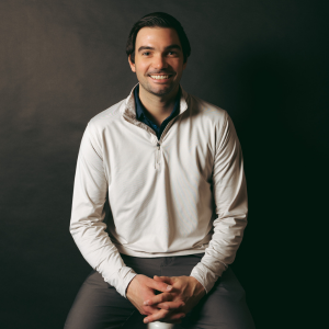 Logan Gruhl smiling at the camera in a cream sweater