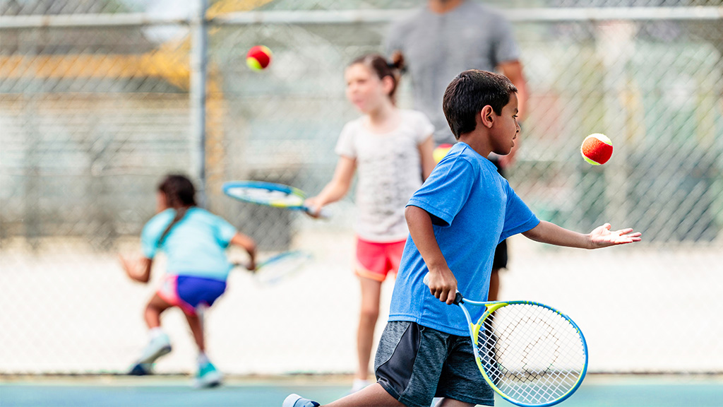 Children playing on a tennis court and hitting a ball in the air.