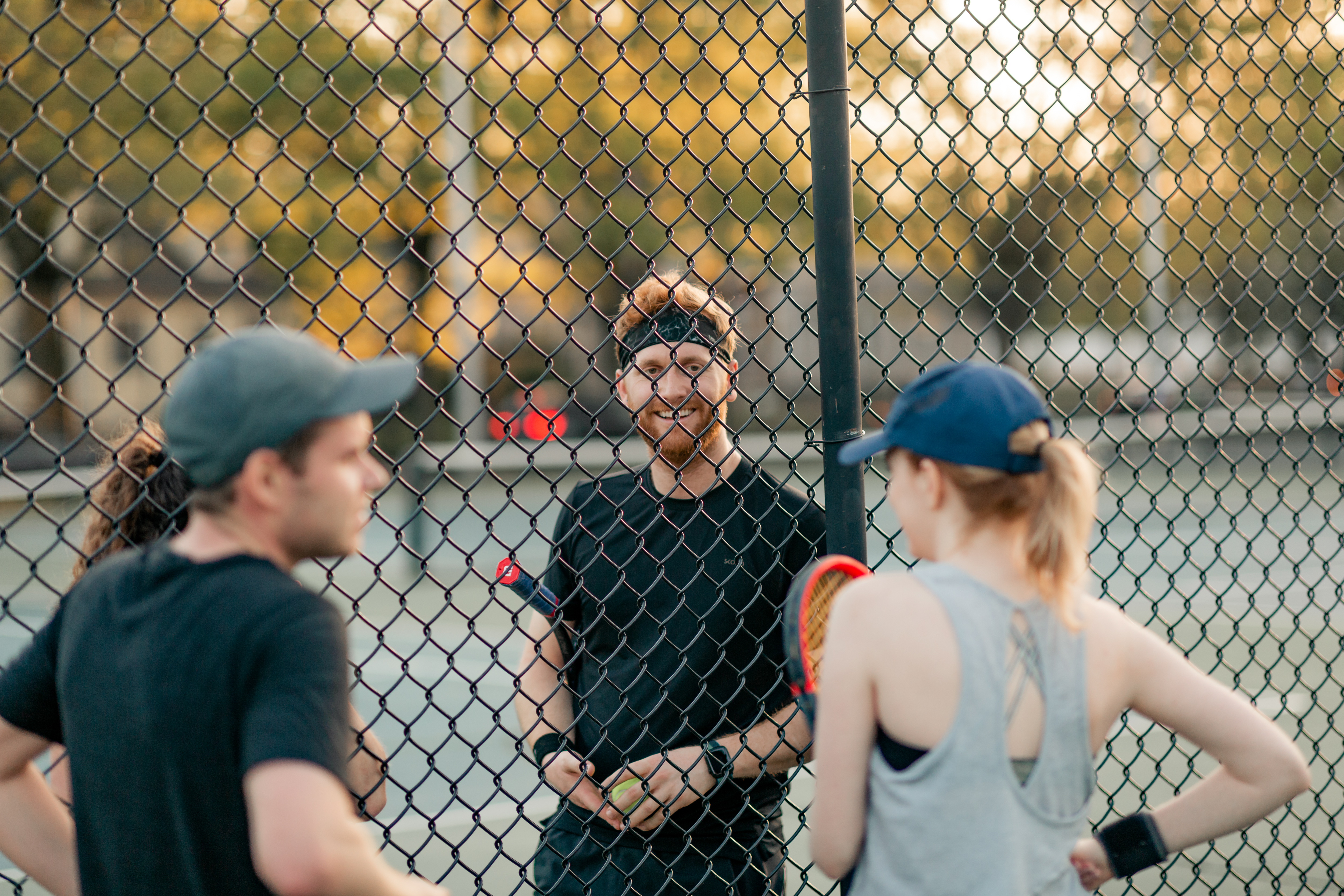 A group of young adults stand in a circle talking with a fence between them.