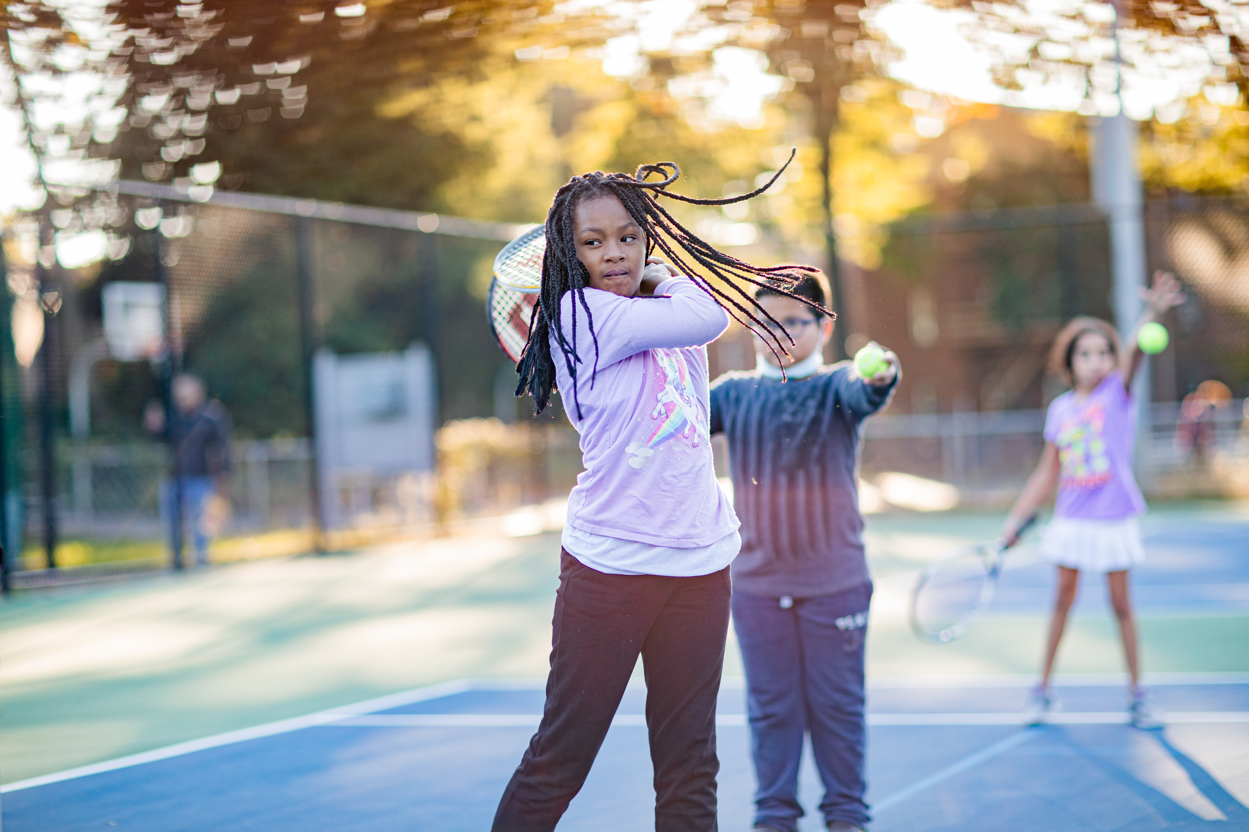 Young girl just finishing a hit stands with her racquet behind her head and her hair flowing from the movement.