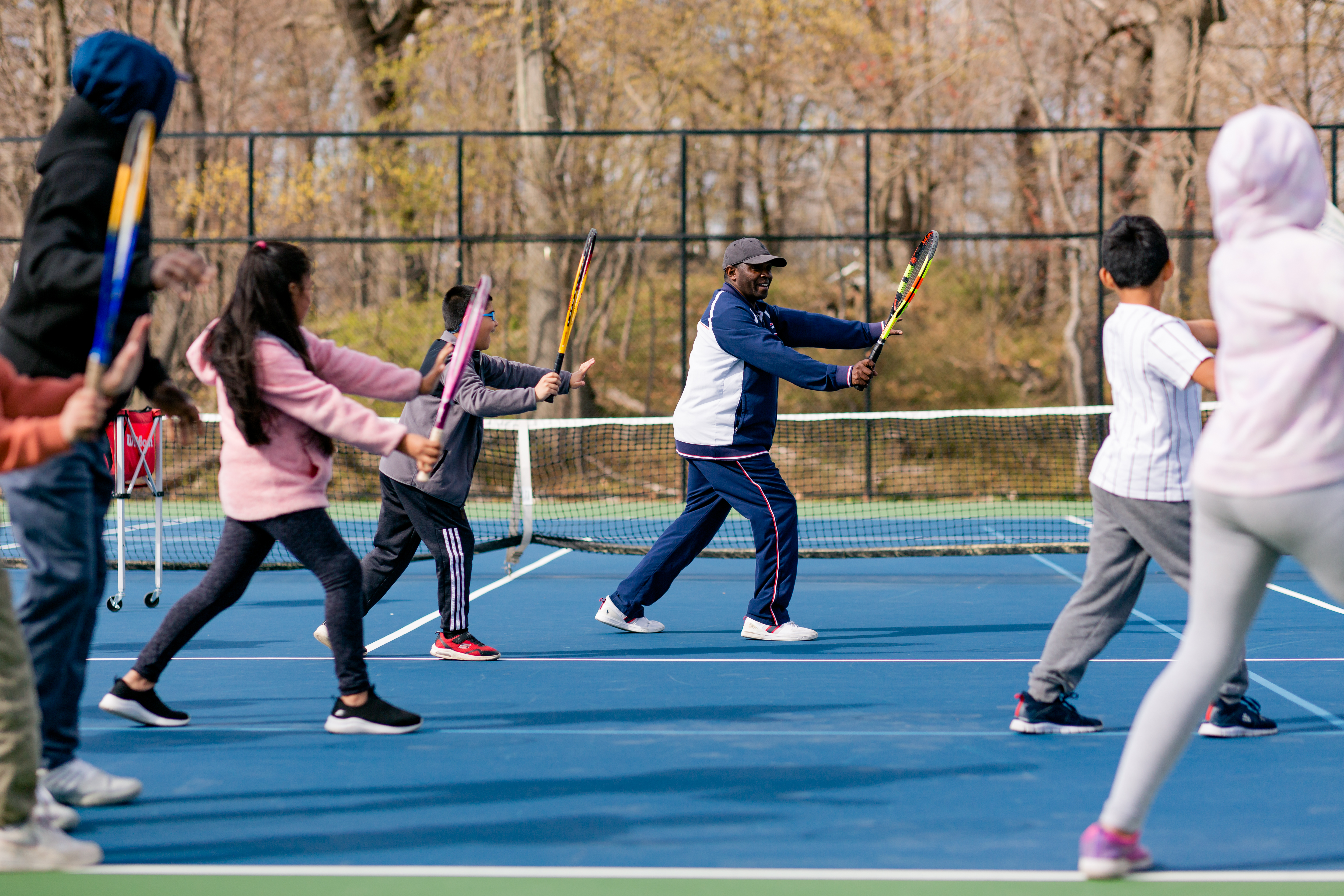 Coach leading a group of children in exercises on the tennis court.