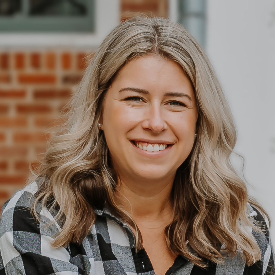 Tara wears a plaid black and white shirt and smiles in a headshot photo.