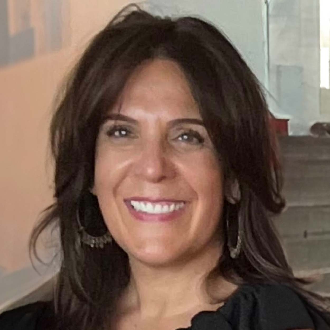 Julie Savanelli smiles warmly in this professional headshot, wearing a black top and hoop earrings.