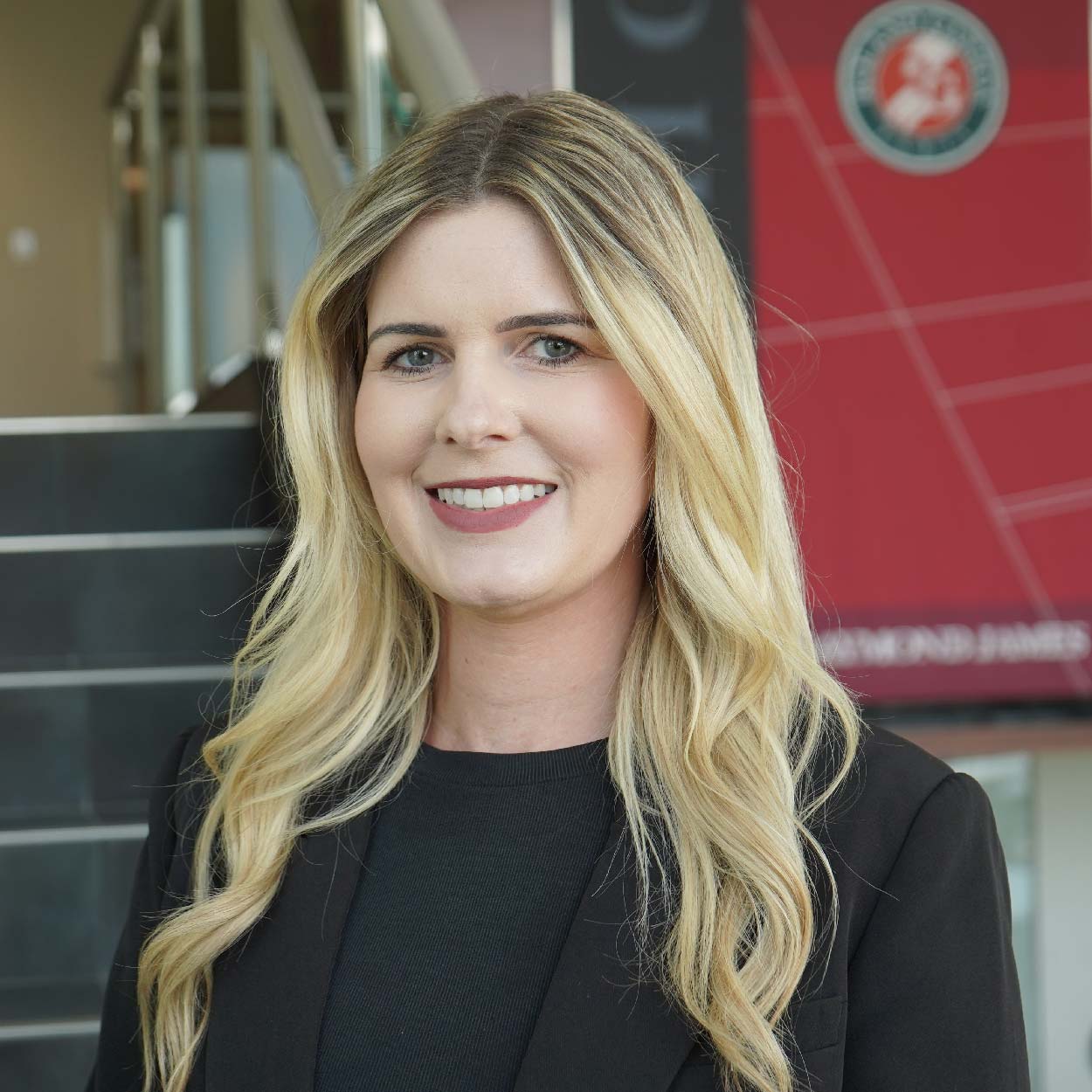A professional headshot of Kristen Ross, smiling confidently in front of a modern indoor setting with a French Open banner in the background.