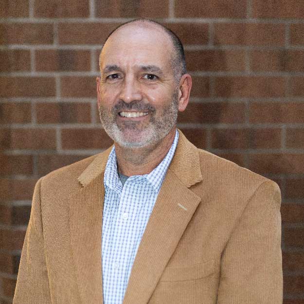 Brian Dean smiling indoors in front of a brick background.