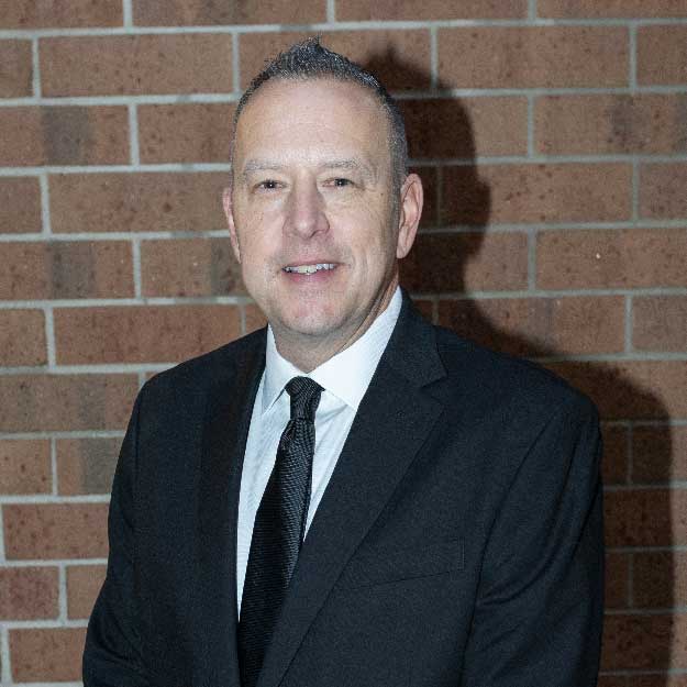 Greg Boyd smiling indoors in front of a brick background.