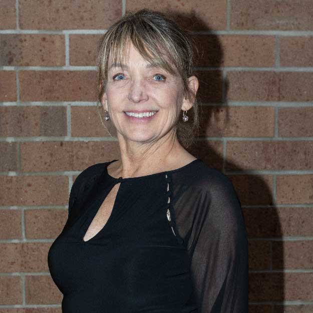 Kim Taylor smiling indoors in front of a brick background.