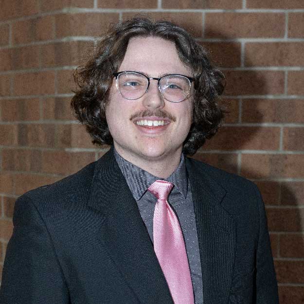 Samuel Stockard smiling indoors in front of a brick background.