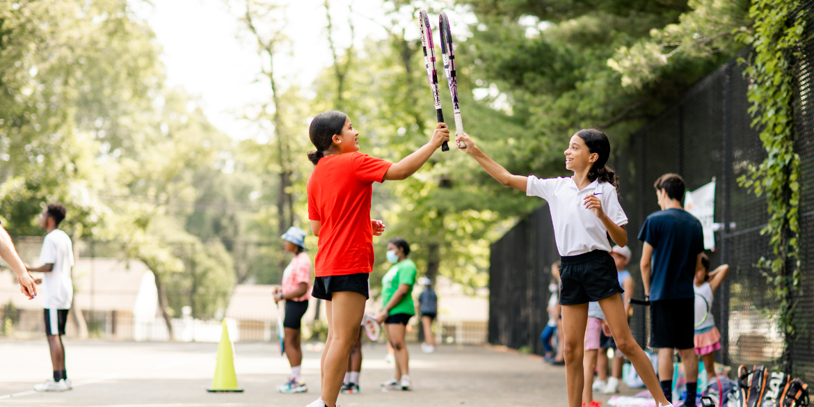 Two girls smiling and tapping their racquets together in excitement.