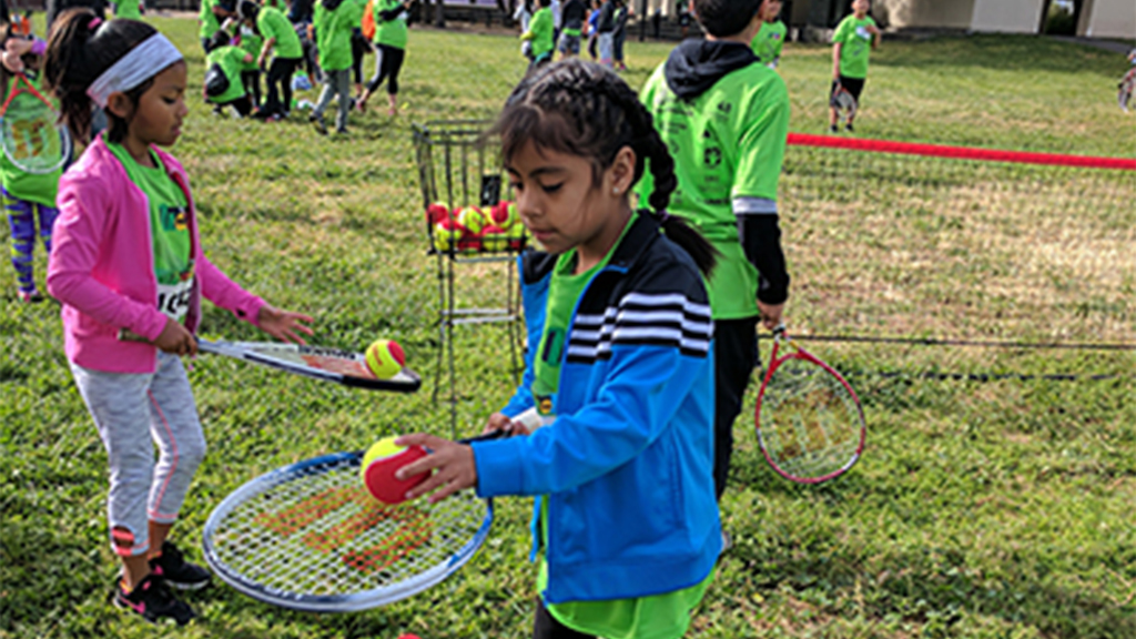 Youth tennis players balancing tennis balls on their racquets.