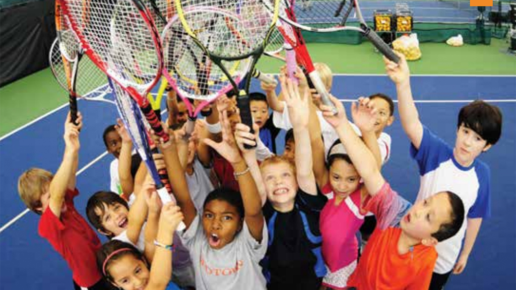 Youth tennis players standing in a tight circle with tennis racquets up in the air.