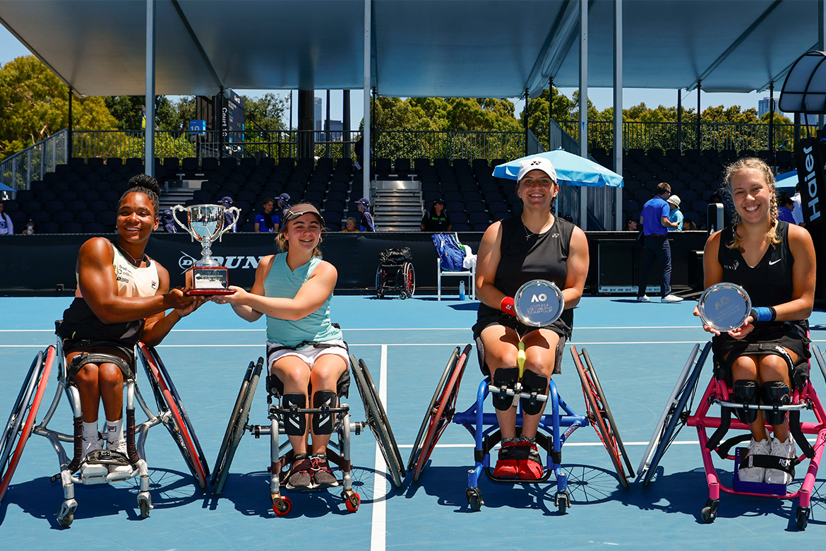Cuatro niñas en sillas de ruedas en una cancha de tenis sostienen trofeos.